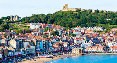 a seafront of Scarborough with houses, a bay and Scarborough Castle on the hill