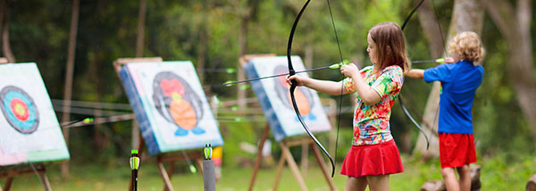 two children using bows to shoot arrows at targets in an archery course