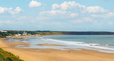 a view of Filey Beach with the tide going out, with Filey Brigg in the background